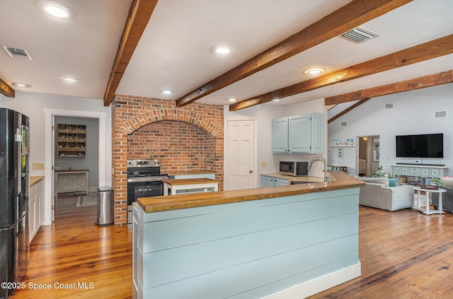 kitchen featuring stainless steel appliances, sink, beamed ceiling, light hardwood / wood-style floors, and butcher block counters