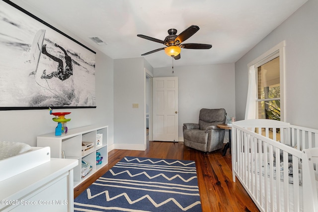 bedroom featuring ceiling fan, dark wood-type flooring, and a nursery area