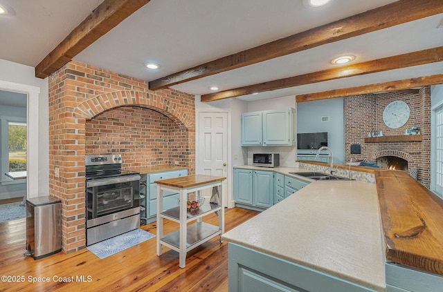 kitchen with stainless steel range with electric cooktop, sink, light hardwood / wood-style flooring, kitchen peninsula, and brick wall