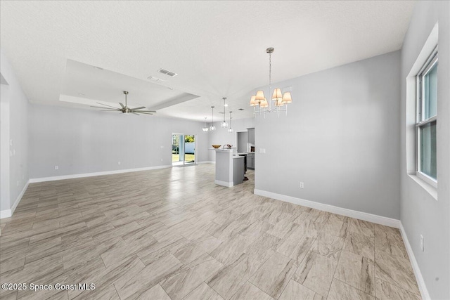 unfurnished living room with a textured ceiling, ceiling fan with notable chandelier, and a tray ceiling