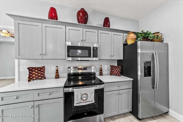 kitchen with gray cabinetry, a textured ceiling, and appliances with stainless steel finishes