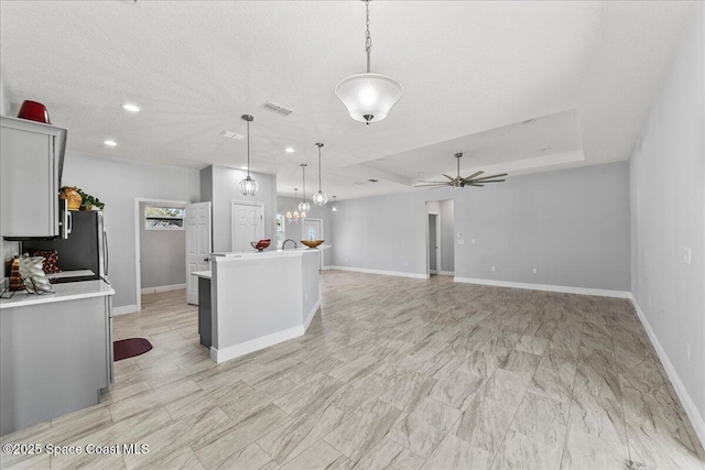 kitchen with ceiling fan with notable chandelier, a textured ceiling, a raised ceiling, pendant lighting, and a kitchen island