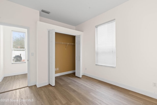 unfurnished bedroom featuring a closet, light hardwood / wood-style floors, and multiple windows