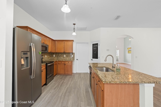 kitchen with an island with sink, sink, hanging light fixtures, light hardwood / wood-style floors, and stainless steel appliances