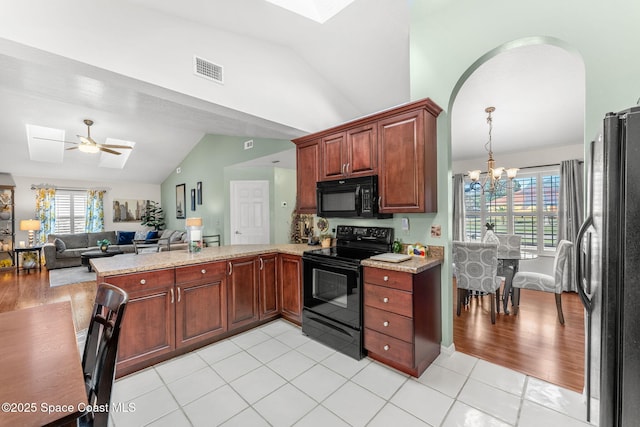 kitchen featuring kitchen peninsula, ceiling fan with notable chandelier, vaulted ceiling, black appliances, and light tile patterned flooring