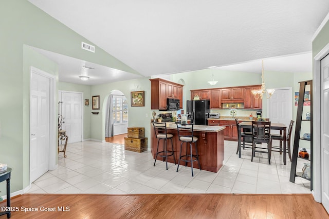 kitchen featuring black appliances, an inviting chandelier, a breakfast bar area, and vaulted ceiling