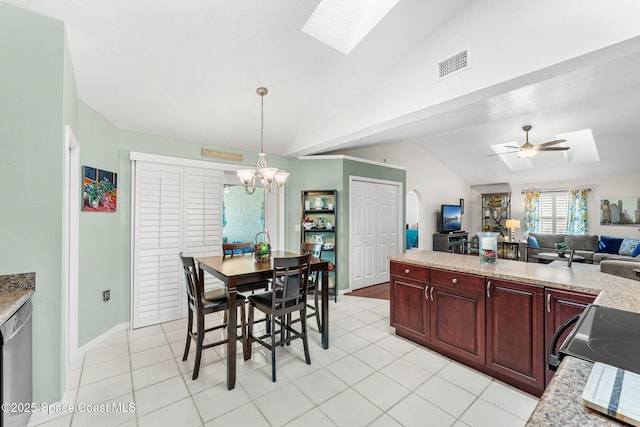 dining space with vaulted ceiling with skylight, ceiling fan with notable chandelier, and light tile patterned floors