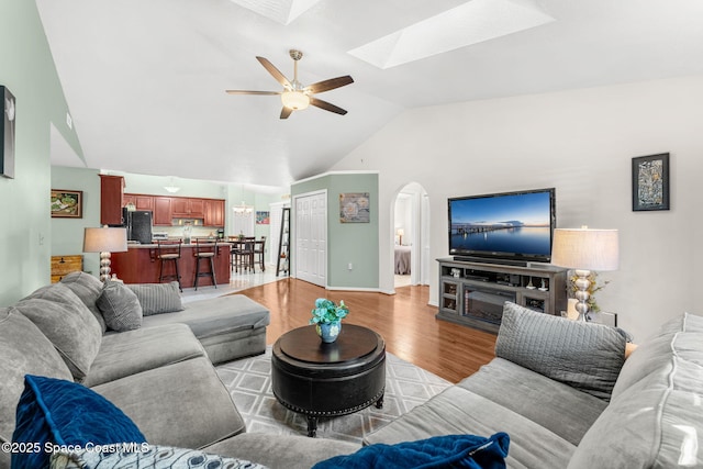 living room featuring light hardwood / wood-style flooring, ceiling fan, and vaulted ceiling with skylight