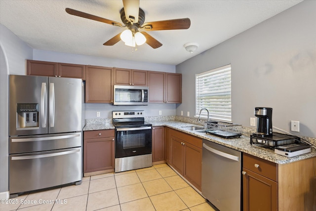 kitchen with ceiling fan, sink, stainless steel appliances, light stone counters, and light tile patterned floors