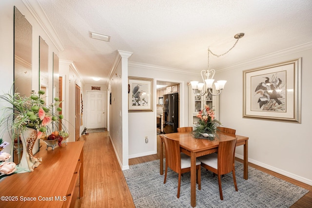 dining space featuring a textured ceiling, hardwood / wood-style floors, crown molding, and a chandelier