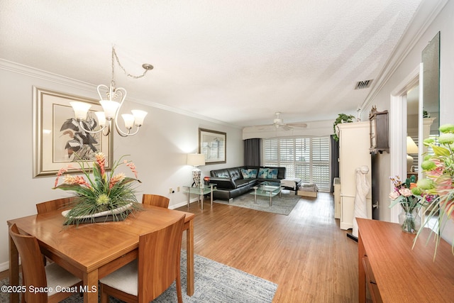 dining space featuring ceiling fan with notable chandelier, a textured ceiling, ornamental molding, and light hardwood / wood-style flooring