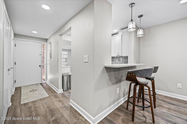 kitchen with a breakfast bar, backsplash, kitchen peninsula, dark hardwood / wood-style flooring, and white cabinetry