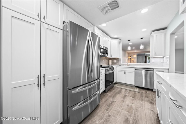 kitchen featuring light stone counters, stainless steel appliances, pendant lighting, white cabinets, and light hardwood / wood-style floors