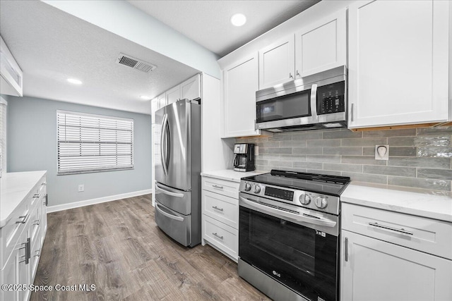 kitchen featuring decorative backsplash, light stone counters, appliances with stainless steel finishes, dark hardwood / wood-style flooring, and white cabinetry