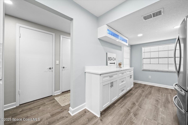 kitchen featuring stainless steel fridge, wood-type flooring, white cabinetry, and a textured ceiling