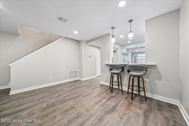 kitchen featuring dark wood-type flooring, hanging light fixtures, a textured ceiling, kitchen peninsula, and a breakfast bar area