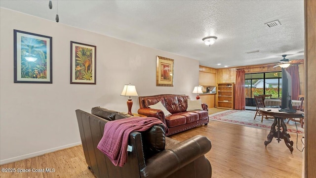 living room with a textured ceiling, light hardwood / wood-style flooring, and ceiling fan