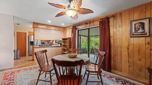 dining area with light wood-type flooring, ceiling fan, wooden walls, and a textured ceiling