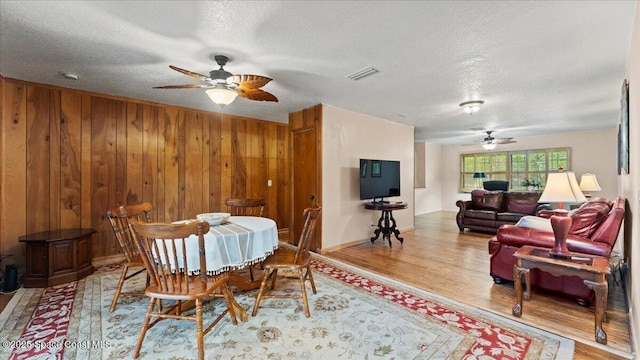 dining room featuring ceiling fan, wooden walls, a textured ceiling, and hardwood / wood-style floors