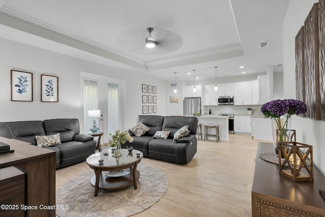 living room featuring a raised ceiling, ceiling fan, and light hardwood / wood-style floors