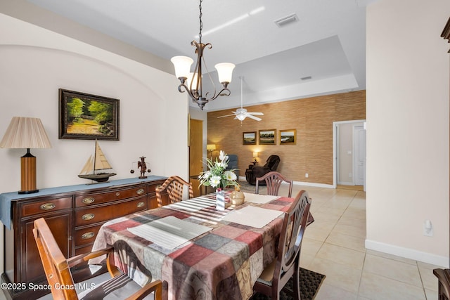 tiled dining area featuring a raised ceiling and ceiling fan with notable chandelier