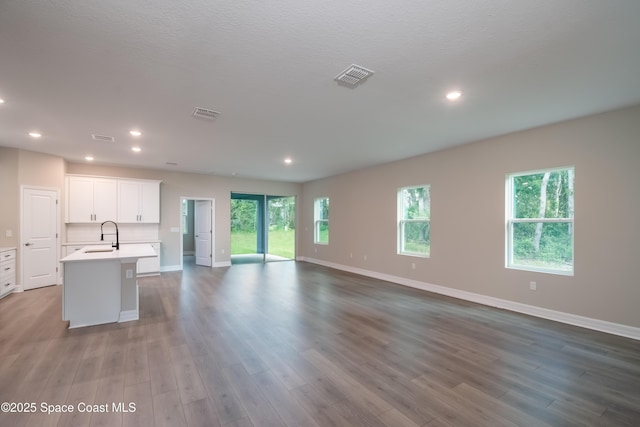 kitchen with sink, a textured ceiling, a kitchen island with sink, white cabinets, and hardwood / wood-style flooring