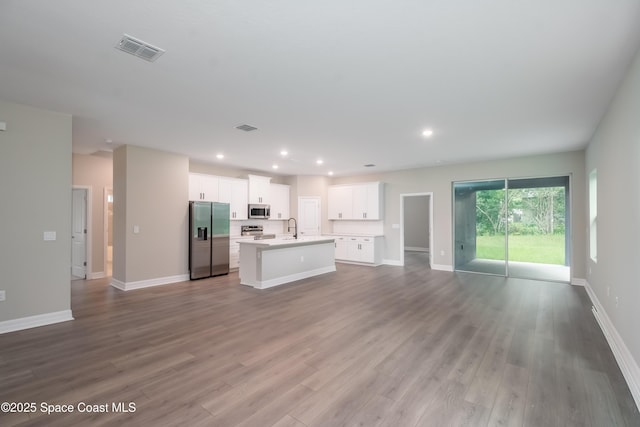 interior space with appliances with stainless steel finishes, sink, light hardwood / wood-style floors, white cabinetry, and an island with sink