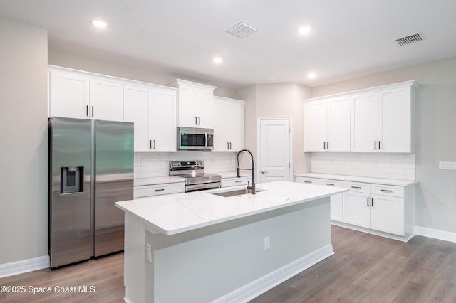 kitchen featuring sink, light stone counters, a center island with sink, white cabinets, and appliances with stainless steel finishes