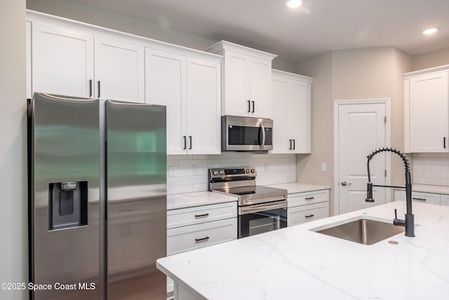 kitchen with white cabinets, appliances with stainless steel finishes, light stone countertops, and sink