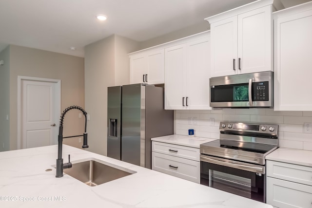 kitchen featuring light stone countertops, appliances with stainless steel finishes, backsplash, sink, and white cabinetry