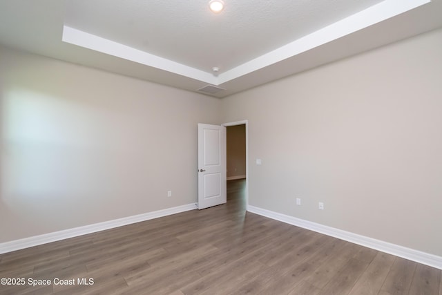 empty room featuring wood-type flooring and a tray ceiling