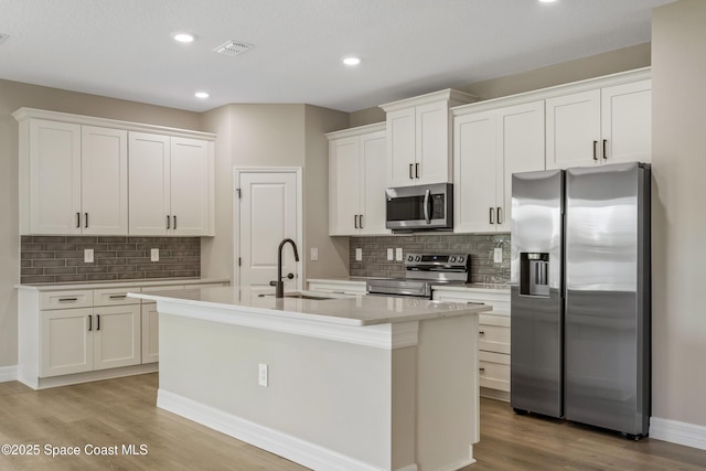 228 Dunlap Ave SE, Palm Bay, FL 32909 - kitchen with an island with sink, light wood-type flooring, a sink, appliances with stainless steel finishes, and backsplash