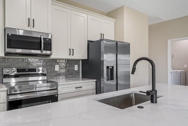228 Dunlap Ave SE, Palm Bay, FL 32909 - kitchen with a sink, separate washer and dryer, stainless steel appliances, white cabinetry, and tasteful backsplash