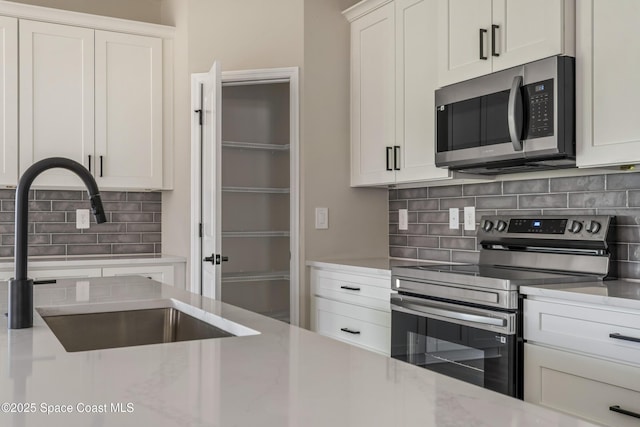 228 Dunlap Ave SE, Palm Bay, FL 32909 - kitchen with white cabinets, light stone countertops, appliances with stainless steel finishes, a sink, and backsplash