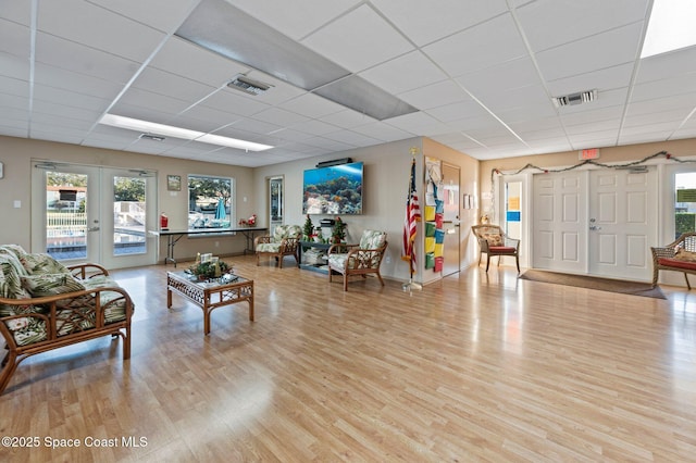 living room featuring a drop ceiling, light wood-type flooring, and french doors