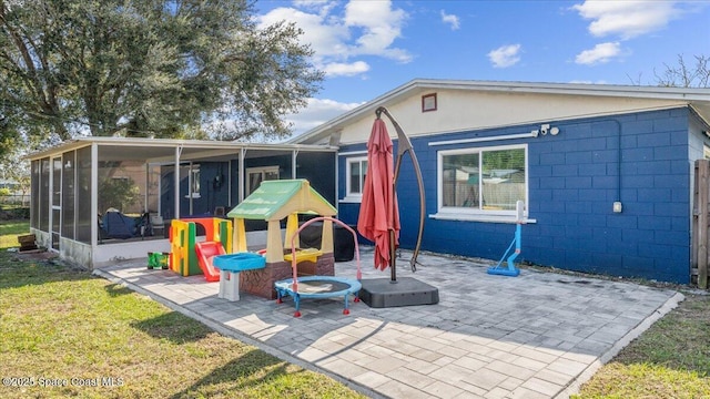 back of property with a sunroom, a playground, a patio, and a lawn