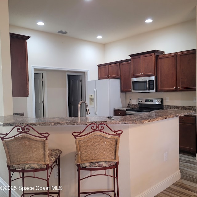 kitchen featuring kitchen peninsula, a kitchen bar, stainless steel appliances, dark stone countertops, and dark hardwood / wood-style floors