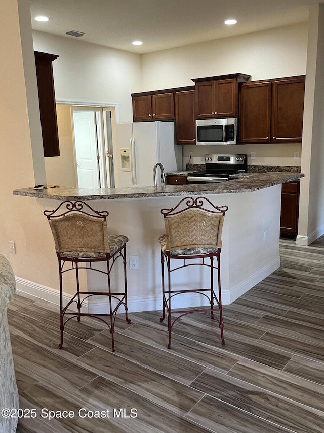 kitchen featuring sink, a kitchen breakfast bar, kitchen peninsula, dark stone countertops, and appliances with stainless steel finishes