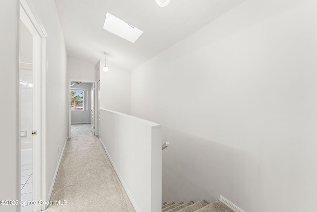 hall with vaulted ceiling with skylight and light colored carpet