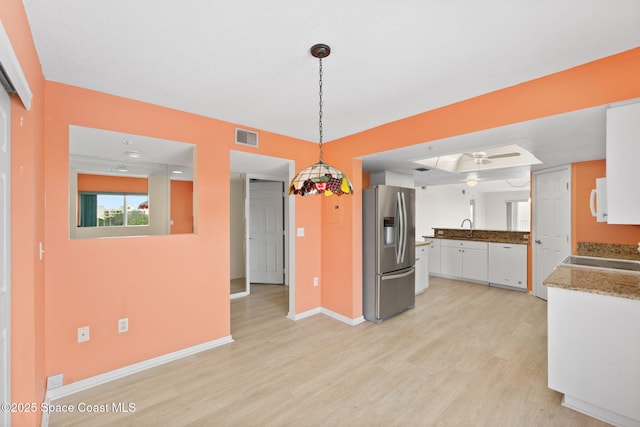 kitchen featuring pendant lighting, stainless steel refrigerator with ice dispenser, white cabinetry, sink, and light hardwood / wood-style flooring