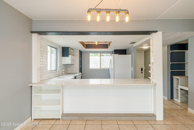 kitchen with white fridge, kitchen peninsula, light tile patterned floors, sink, and tasteful backsplash