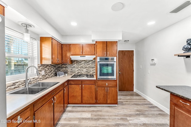 kitchen featuring tasteful backsplash, sink, hanging light fixtures, light hardwood / wood-style floors, and stainless steel appliances