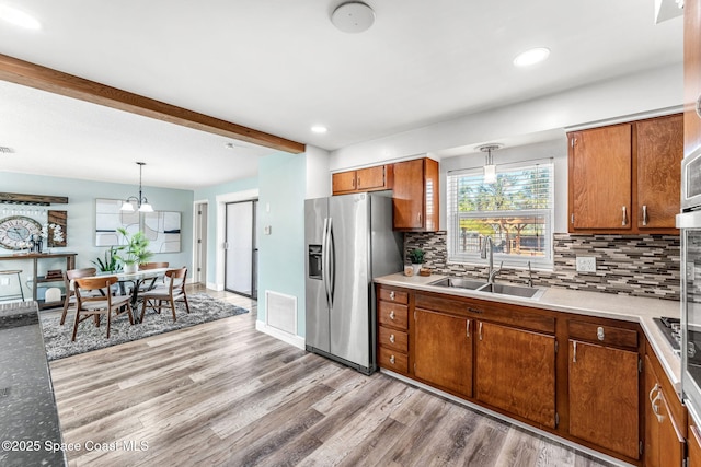 kitchen featuring sink, pendant lighting, backsplash, and stainless steel fridge with ice dispenser