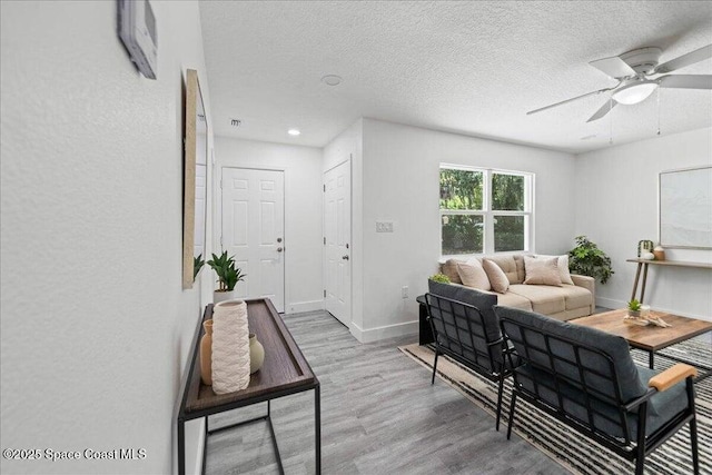 living room featuring ceiling fan, light wood-type flooring, and a textured ceiling