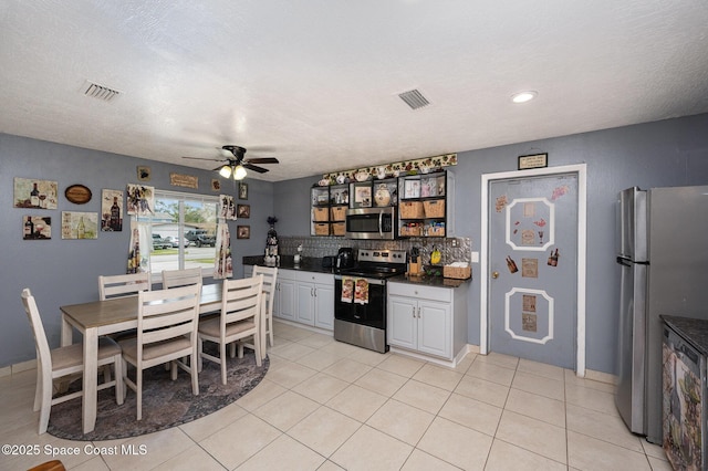 kitchen featuring a textured ceiling, light tile patterned floors, backsplash, appliances with stainless steel finishes, and ceiling fan