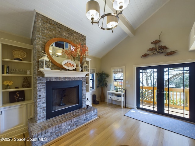 unfurnished living room with french doors, light hardwood / wood-style flooring, a brick fireplace, built in shelves, and a notable chandelier