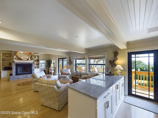 kitchen featuring a fireplace, light hardwood / wood-style flooring, built in features, beamed ceiling, and white cabinetry