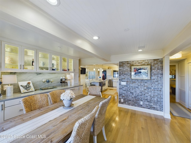 dining area with light hardwood / wood-style floors, beam ceiling, and brick wall