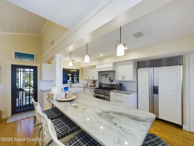 kitchen featuring high quality appliances, tasteful backsplash, decorative light fixtures, light stone counters, and white cabinetry