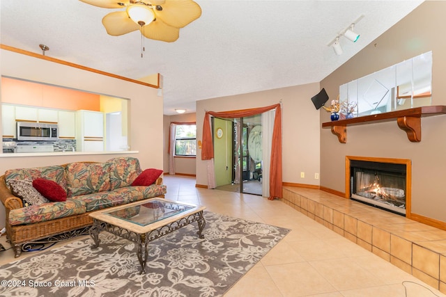 tiled living room with a textured ceiling, track lighting, ceiling fan, and a tiled fireplace